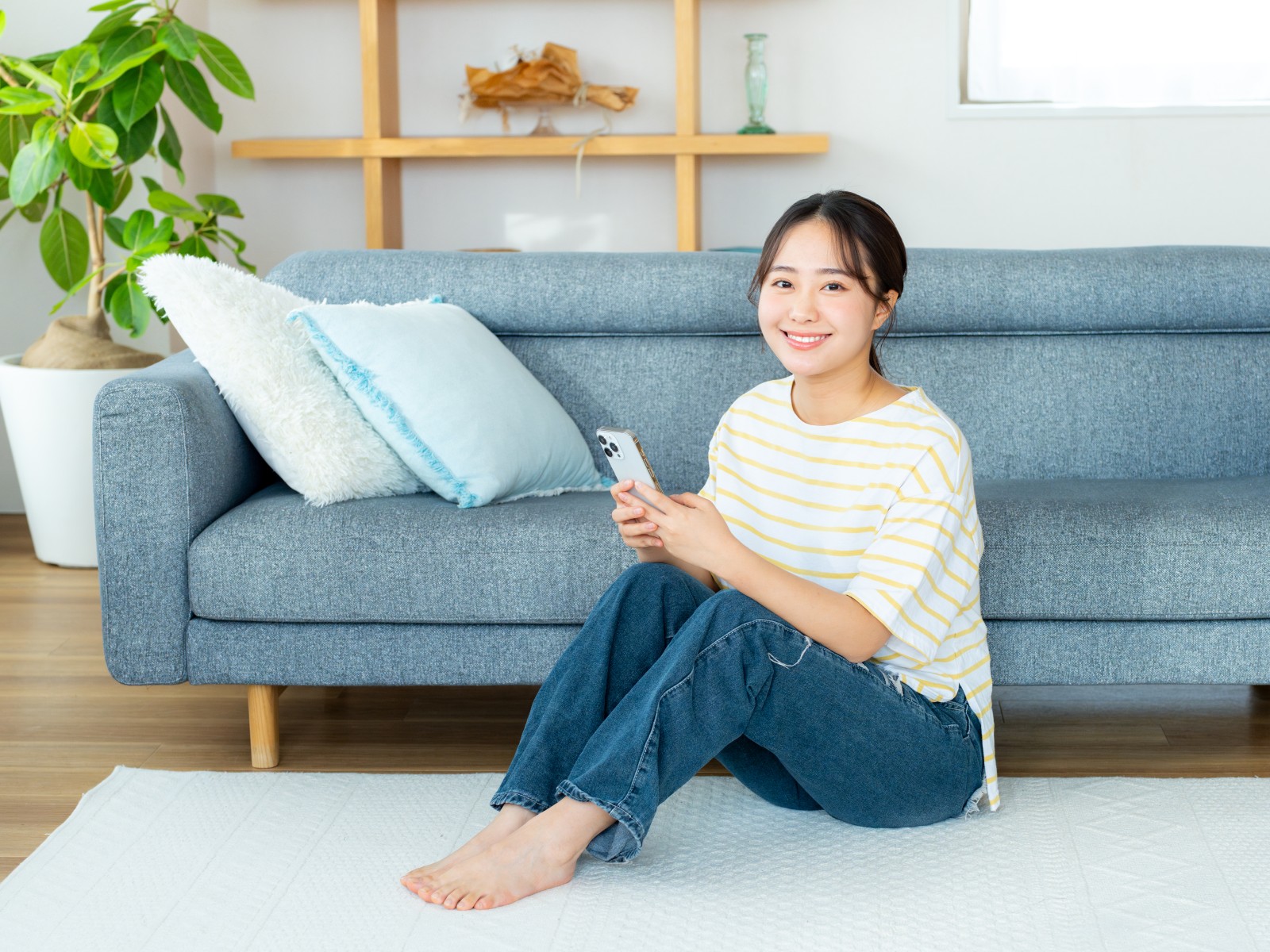 リビングでスマホを片手に微笑む女性