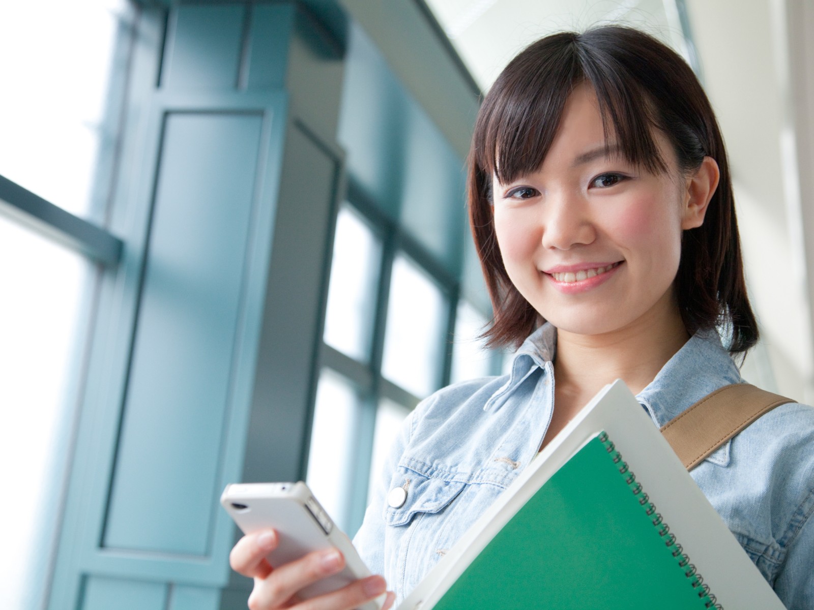 大学の廊下でスマホを片手に微笑む女性